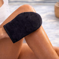 Black velvet self tanning applicator mitt applying self tanner to smooth, sun-kissed skin for an even, streak-free glow.