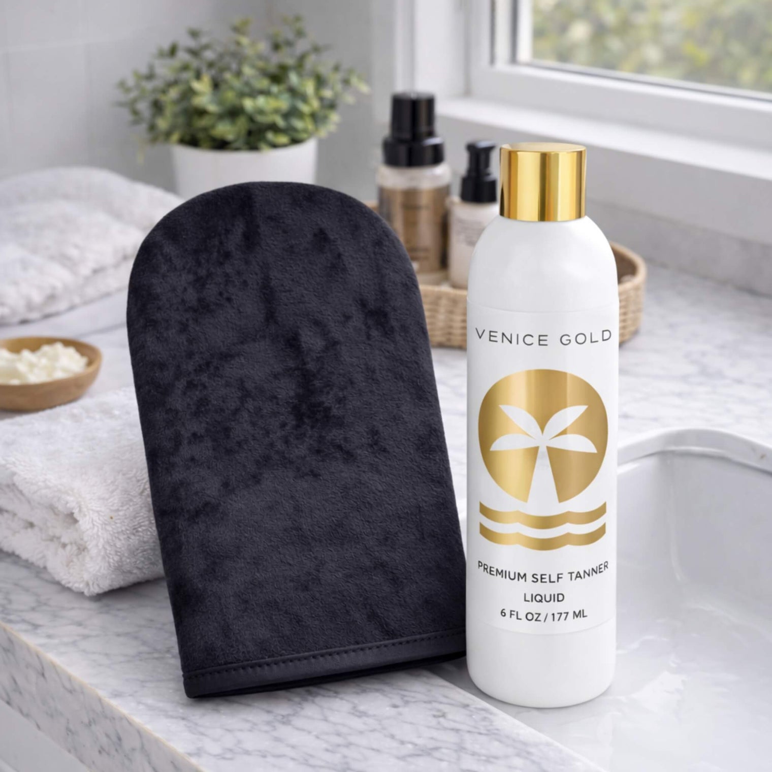 Venice Gold self tanning applicator mitt paired with Venice Gold Premium Self Tanner on a marble bathroom countertop.